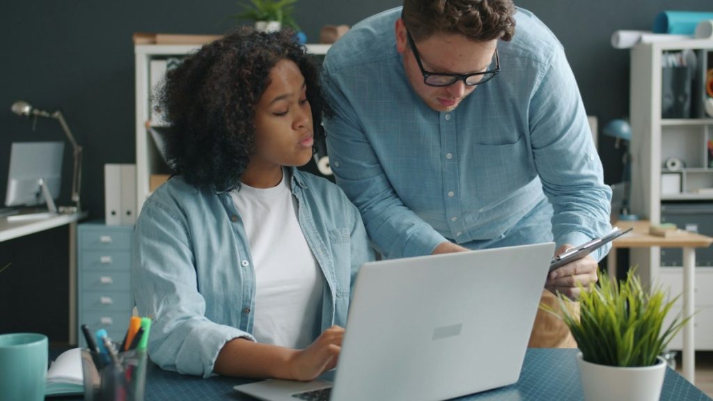 An experienced colleague coaching a team member at a laptop