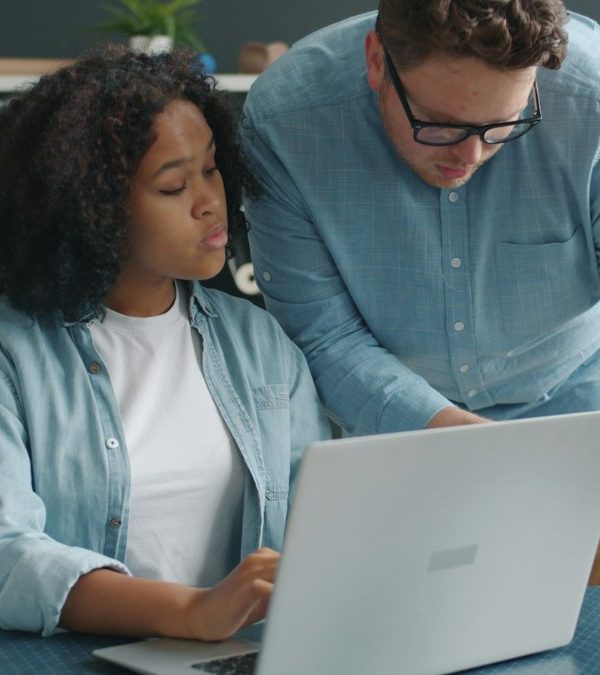 An experienced colleague coaching a team member at a laptop